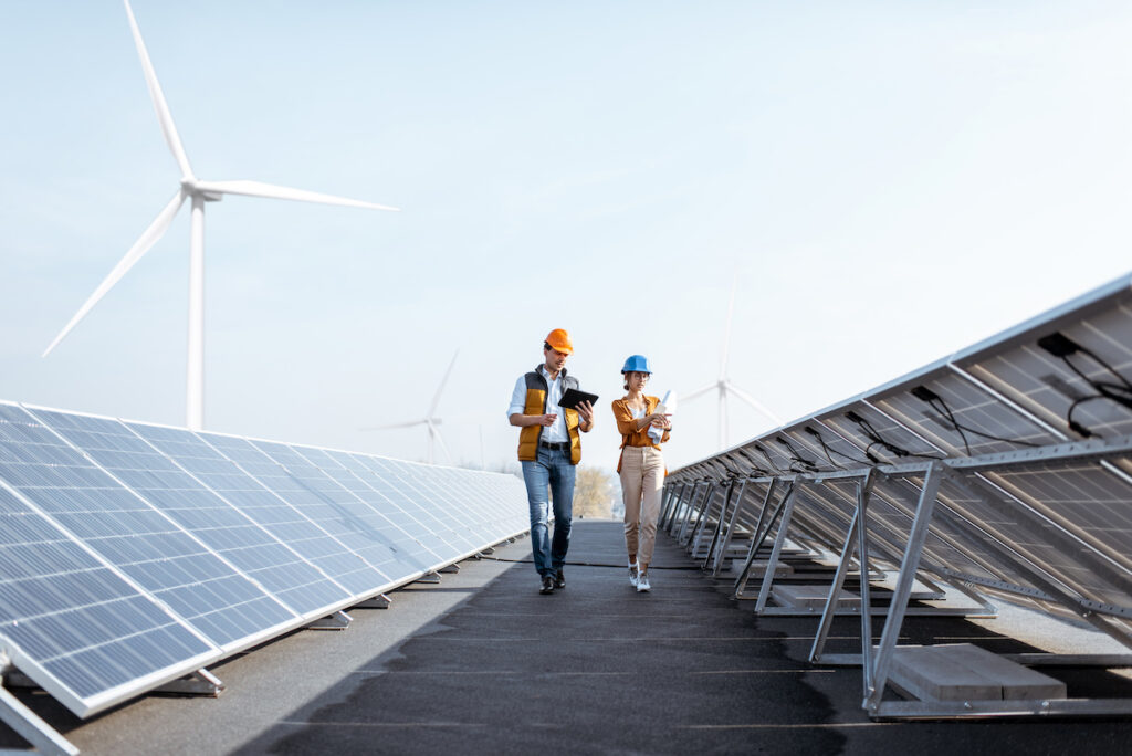 View on the rooftop solar power plant with two engineers walking and examining photovoltaic panels.